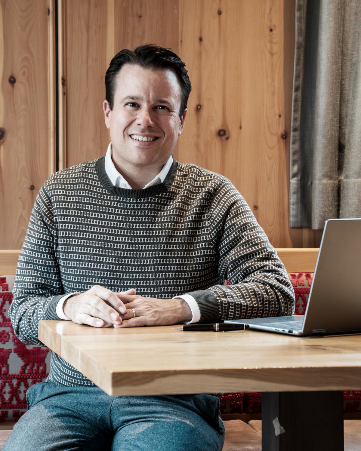 Florian Mascarello, lachend am Tisch in der Gaststube des Dechbettener Hofs, vor sich ein aufgeklappter Laptop